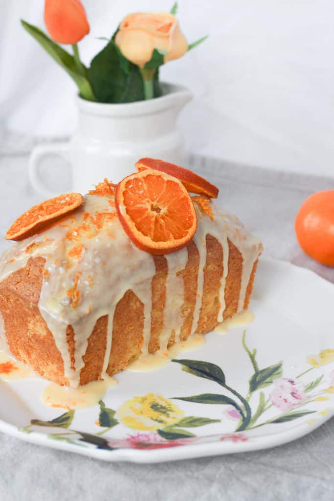 easy clementine bread topped with a glaze and dried oranges on a floral plate