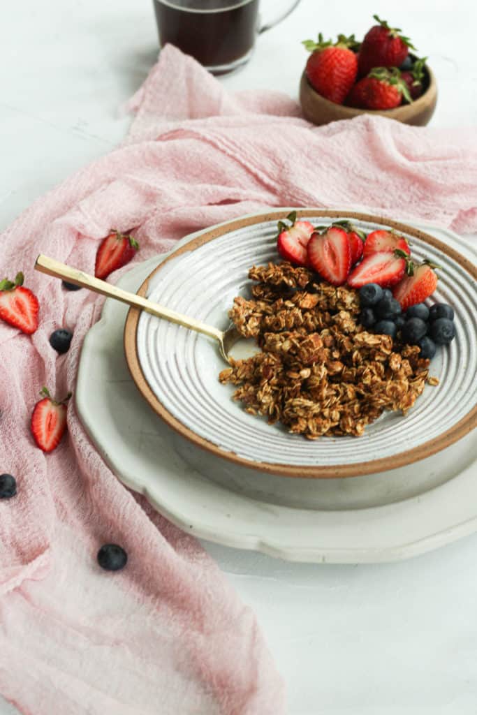 granola with berries and milk in a gray bowl with a gold spoon