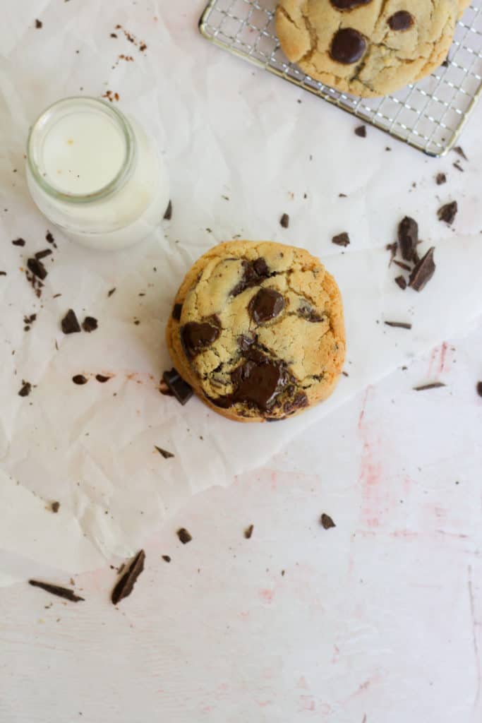 look down on stack of chocolate chip cookies with a milk bottle on a pink backdrop