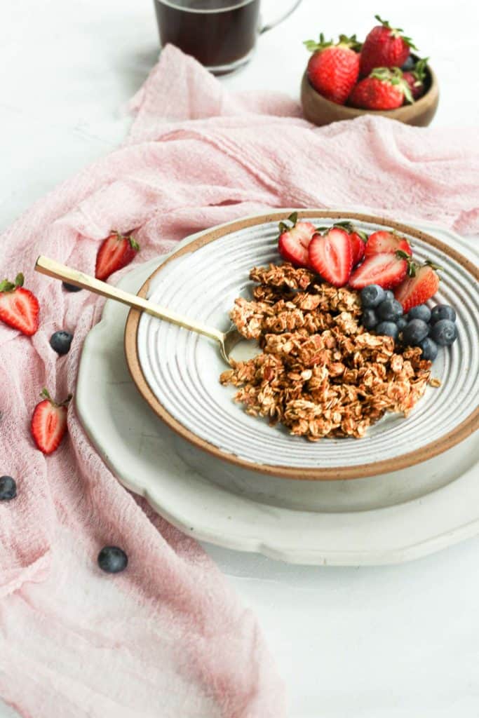healthy vegan granola without oil in bowl with berries and gold spoon.