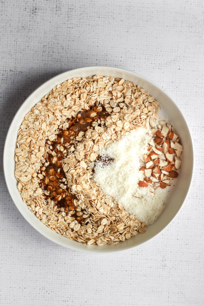 maple syrup, oats, coconut, and almonds in a white bowl