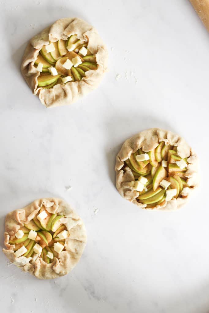 three uncooked apple galettes with butter pieces