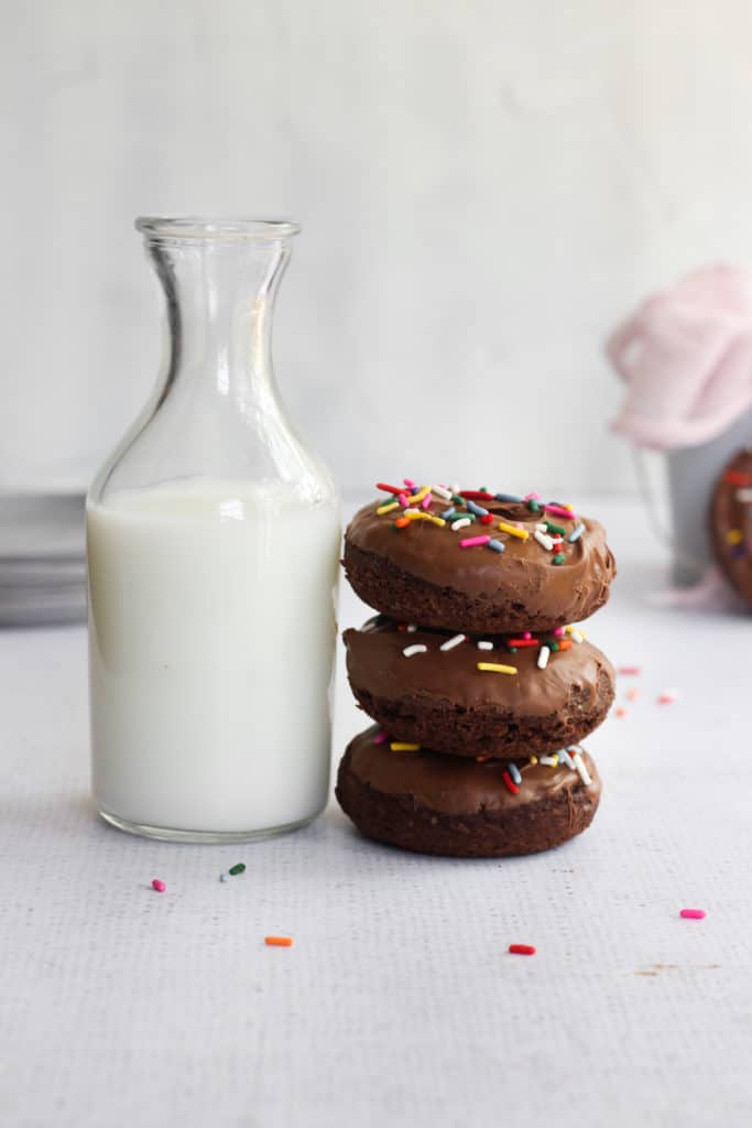stack of baked double chocolate cake donuts with a pitcher of milk