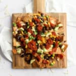 loaded air-fryer nachos on a square wood board on a white backdrop