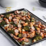 sheet pan full of roasted vegetables and chicken sausage with a white napkin on a white backdrop