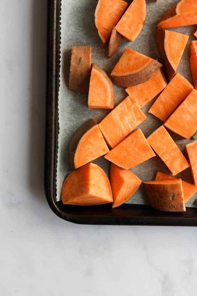 Sheet pan corner lined with parchment paper, cubed sweet potatoes on top of parchment