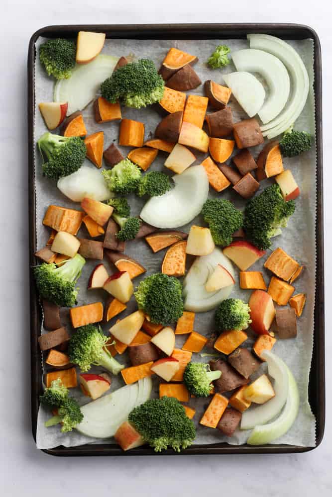 parchment paper lined sheet pan filled with sweet potatoes, broccoli, onions, and apples