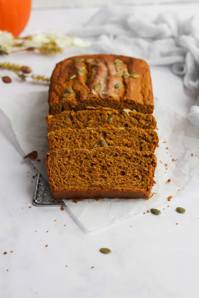 pumpkin bread with three slices on parchment paper on white backdrop