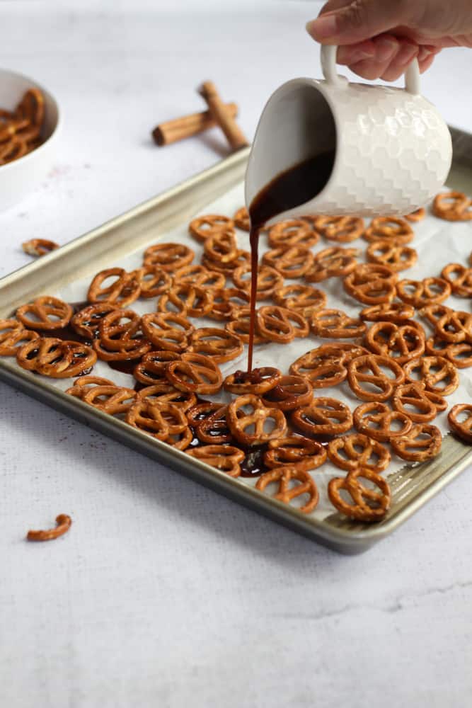 pretzels on a sheet pan lined with parchment paper with hand pouring syrup over top
