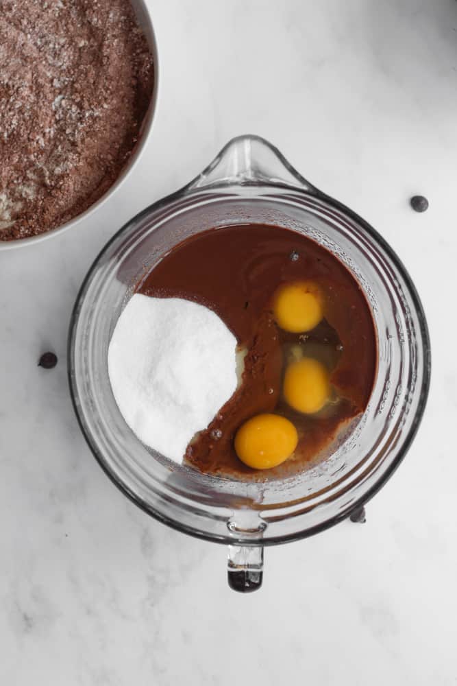 sugar and eggs in a bowl of melted chocolate and butter on a white backdrop