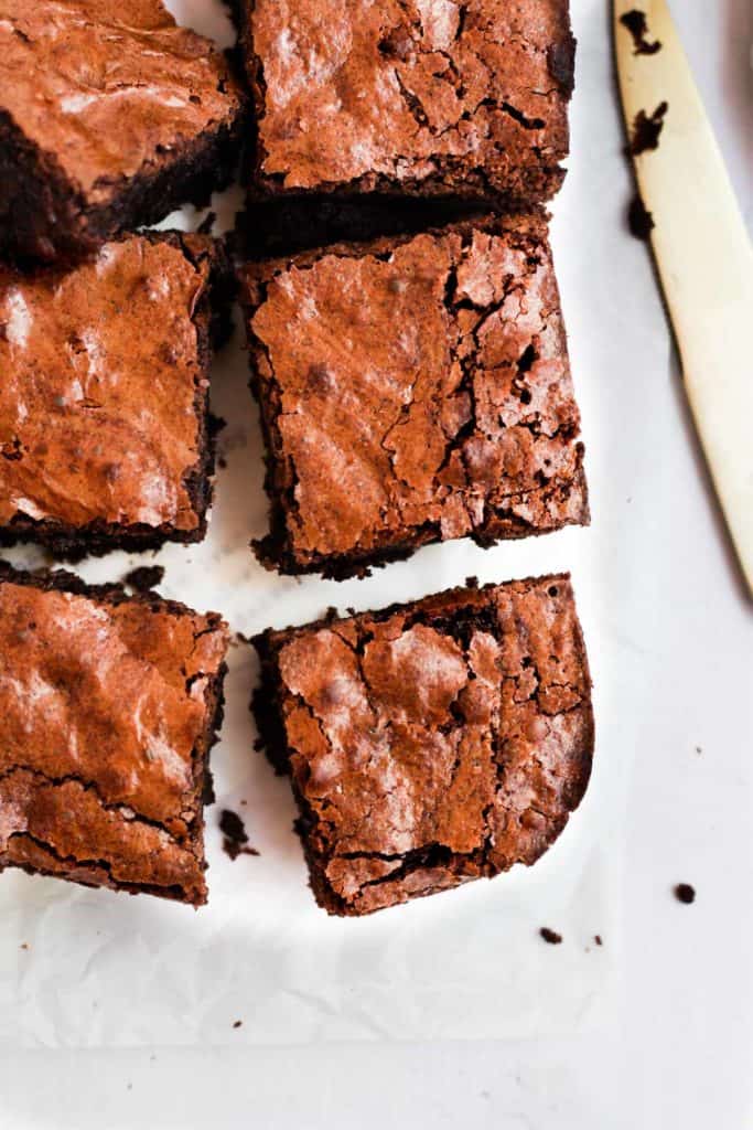 brownies with a shiny top cut into squares on parchment paper.
