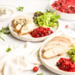 turkey tenderloin cooked on white plate with salad, butter, and cranberries.