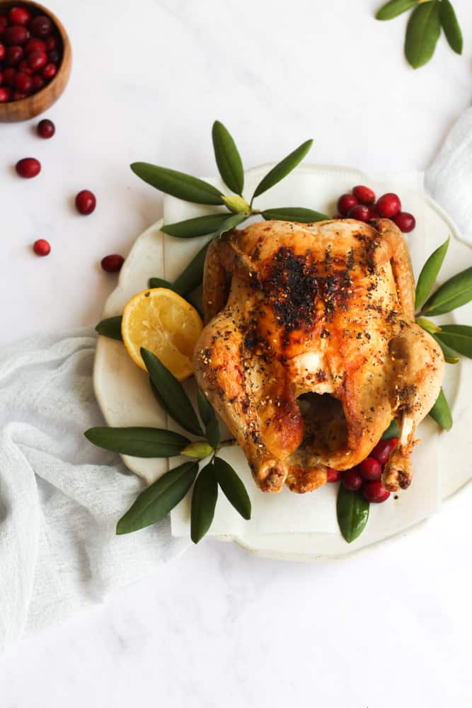 air fryer whole chicken on a white plate with green leaves and cranberries