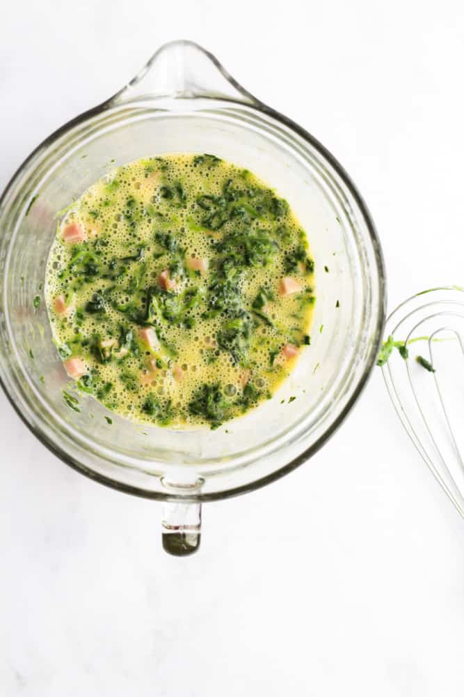 eggs, ham and spinach in a large glass bowl on a white backdrop