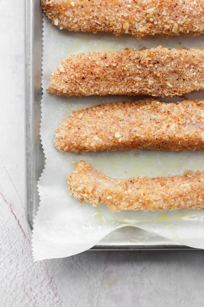breaded chicken on parchment paper lined sheet pan