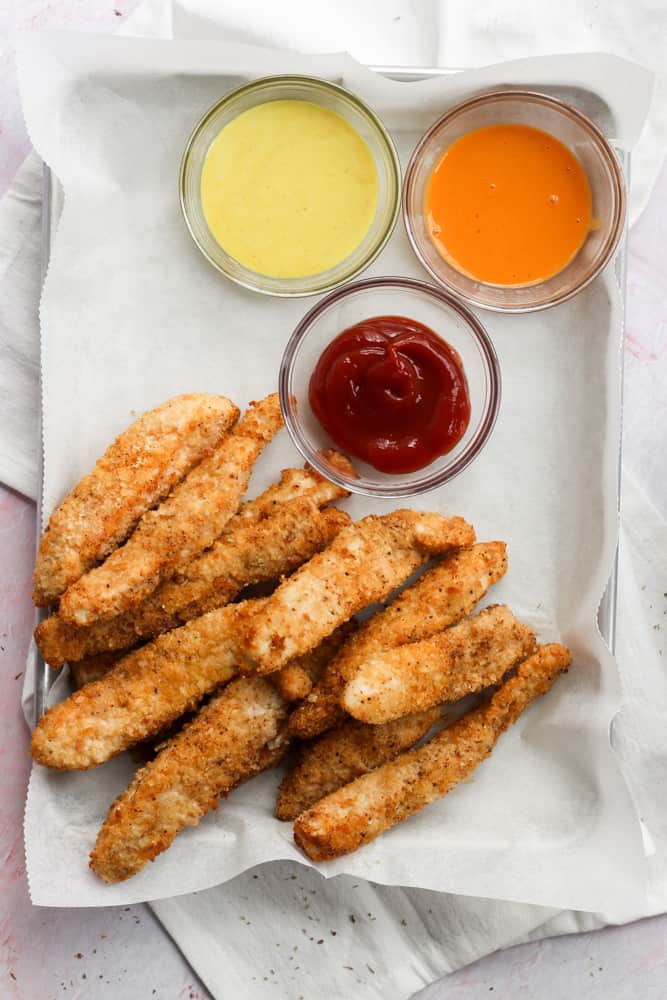 chicken tenders with three dipping sauces on a sheet pan