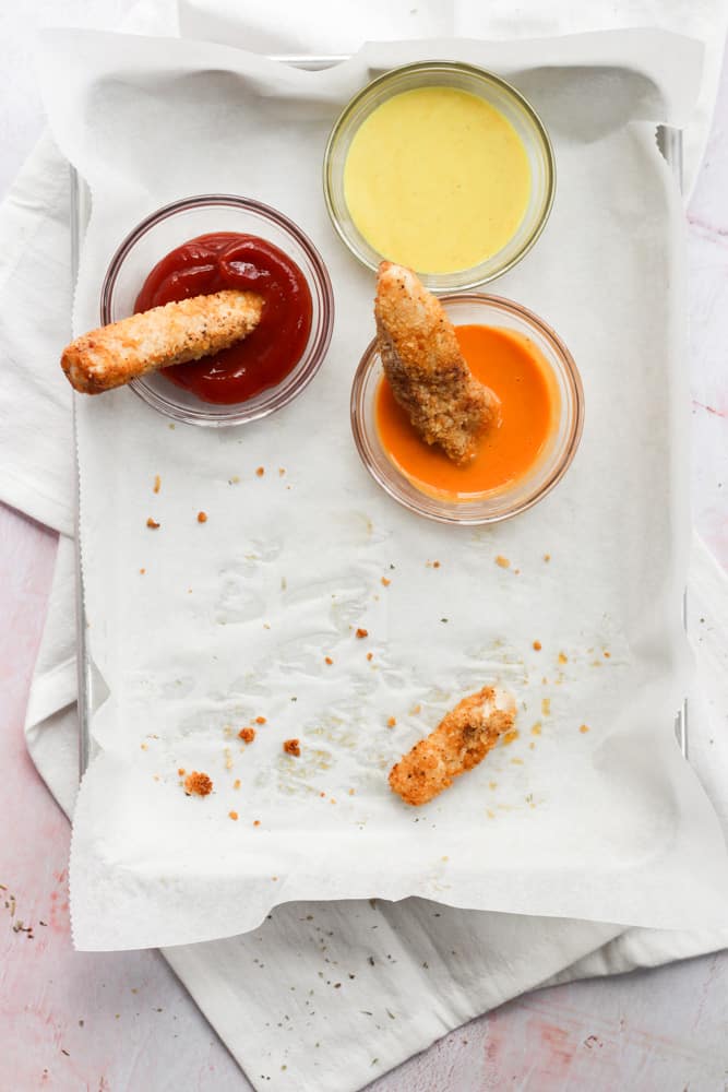 air fryer chicken tenders on a parchment lined baking sheet with 3 dipping sauces