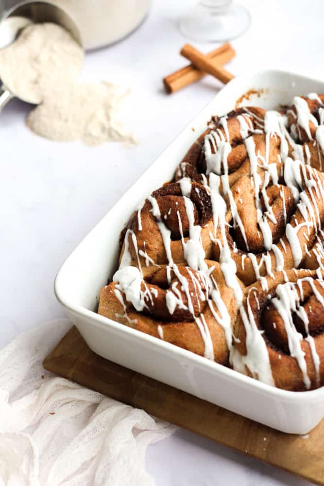 healthy cinnamon rolls on a white baking dish drizzled with vanilla glaze on a white backdrop