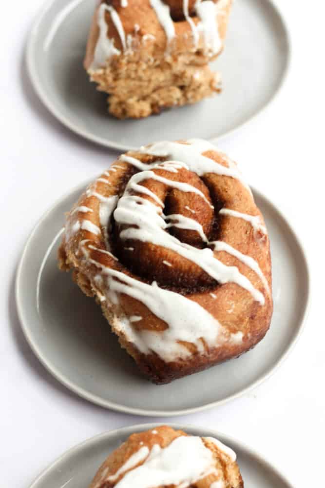 healthier cinnamon roll drizzled with a vanilla glaze on a gray plate on a white backdrop
