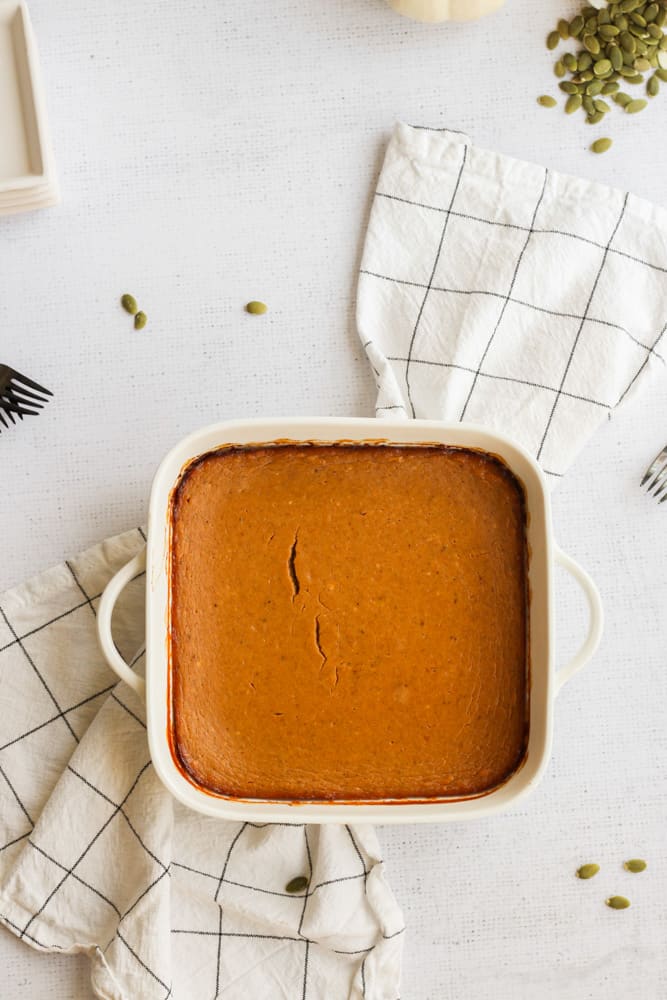 healthy pumpkin pie bars in a square white baking dish on a white and gray linen