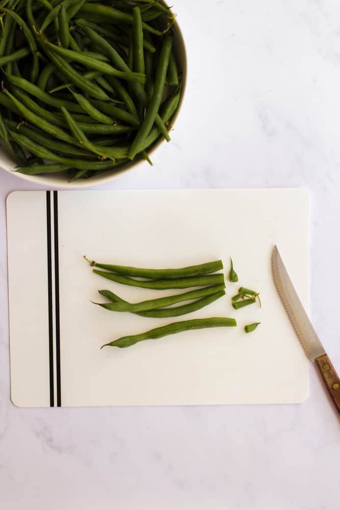 green beans being cut on a white cutting board