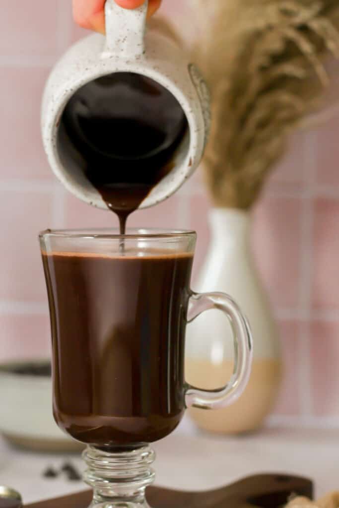 keto hot chocolate being poured into a glass mug.