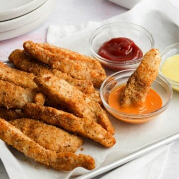 gluten free chicken tenders on a parchment lined sheet tray with 3 dipping sauces.