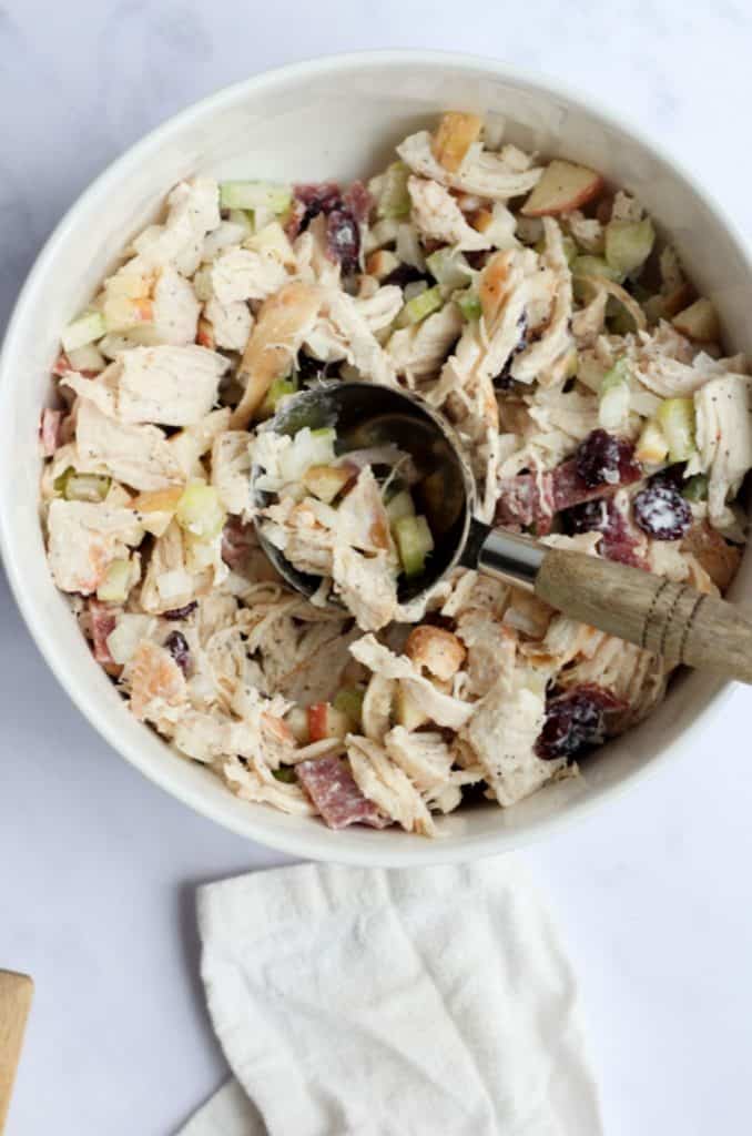 Healthy turkey salad in a white bowl with a wooden scoop