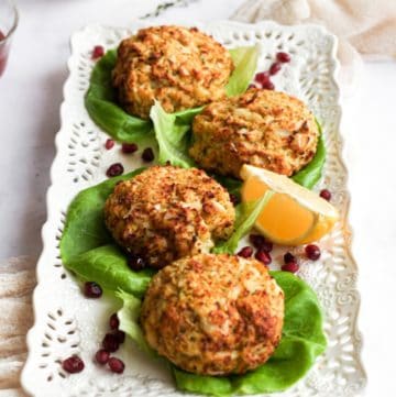 gluten free crab cakes on white tray lined with lettuce, pomegranate seeds, and a lemon wedge