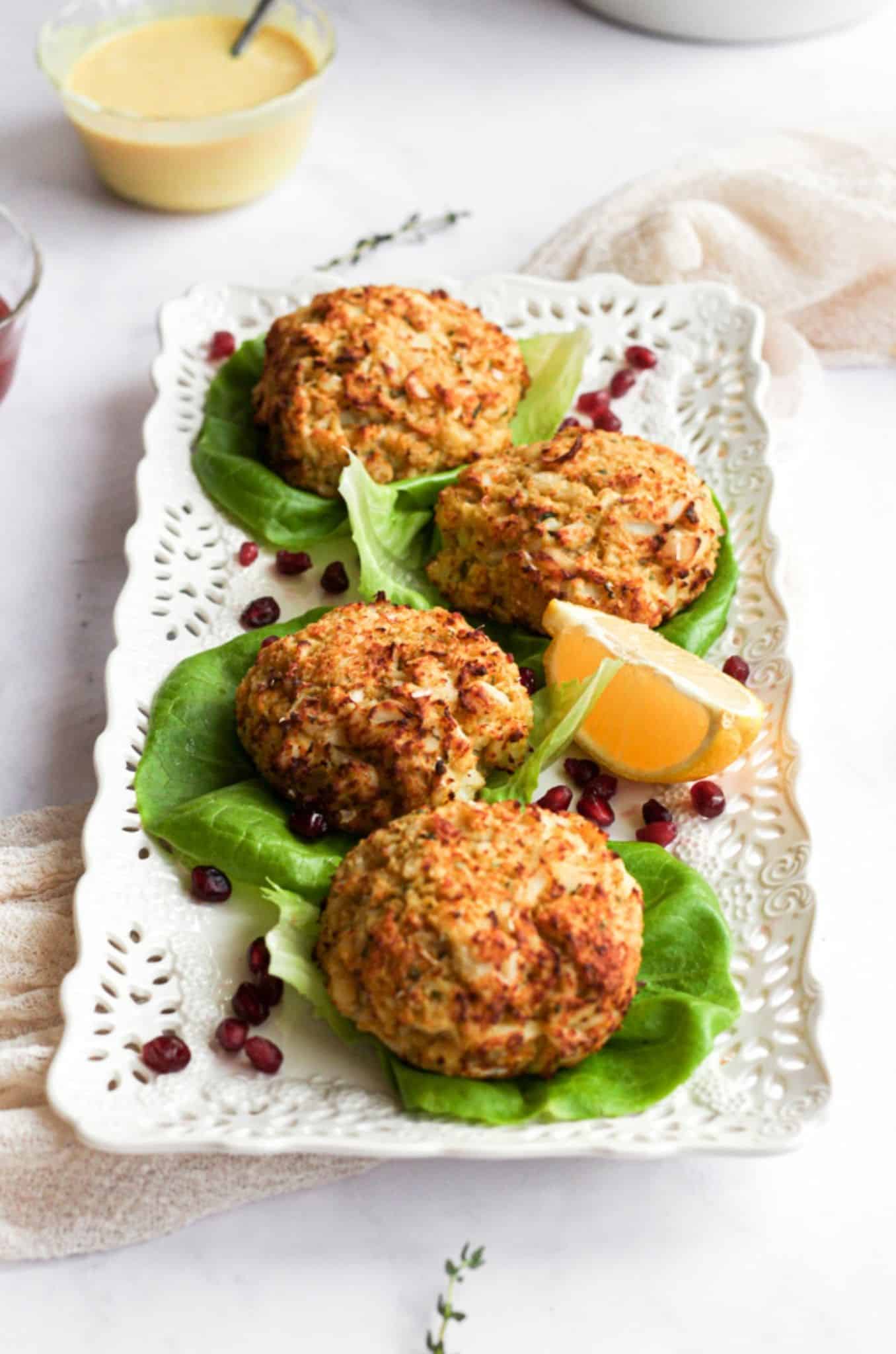 gluten free crab cakes on white tray lined with lettuce, pomegranate seeds, and a lemon wedge