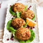 Gluten Free Crab Cakes on a white tray lined with lettuce and pomegranate seeds on a white backdrop