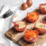 healthy ham and egg cups topped with melted cheese on a wood board with a white napkin
