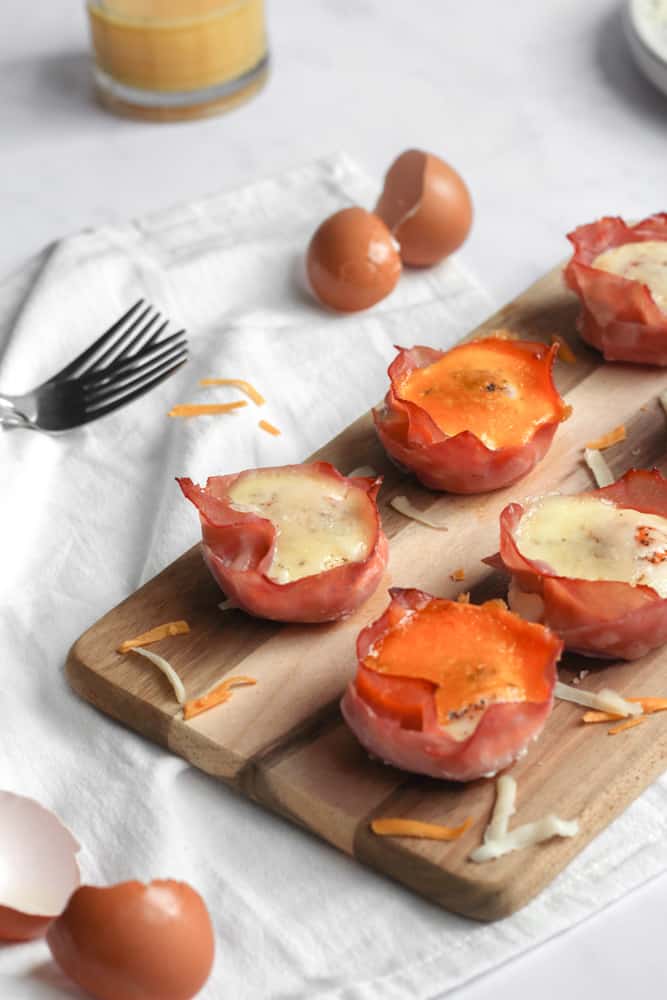 healthy ham and egg cups topped with cheese on a wood board