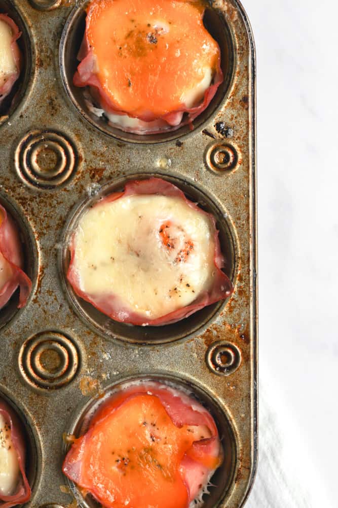 healthy ham and egg cups topped with cheese in a gray muffin tin