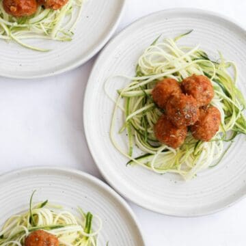 air fryer turkey meatballs on top of zucchini noodles on white plates.