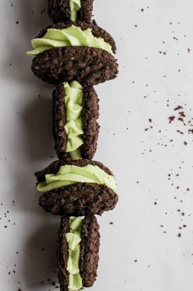 mint chocolate sandwich cookies on their sides in a zig zag pattern on a white backdrop with cookie crumbs to the right of the frame