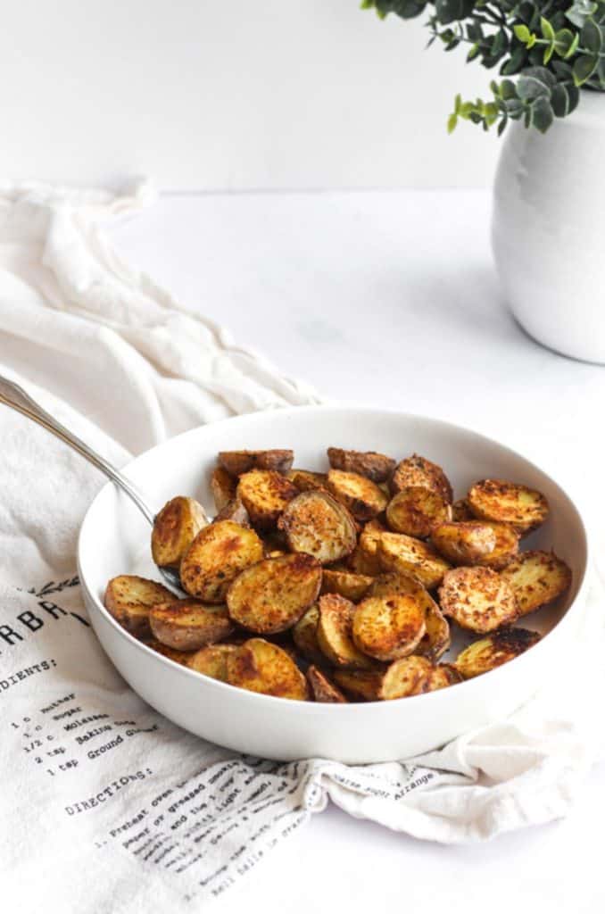 roasted Cajun potatoes in a white bowl with a silver spoon on a white linen