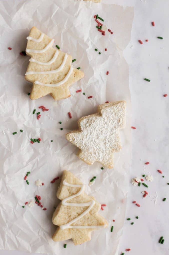 sugar free sugar cookies in Christmas tree shapes on parchment paper with sprinkles