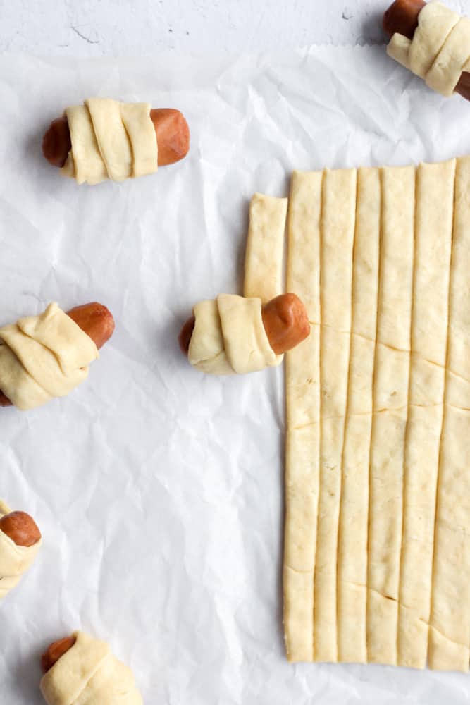 mini sausages being rolled up in crescent roll dough