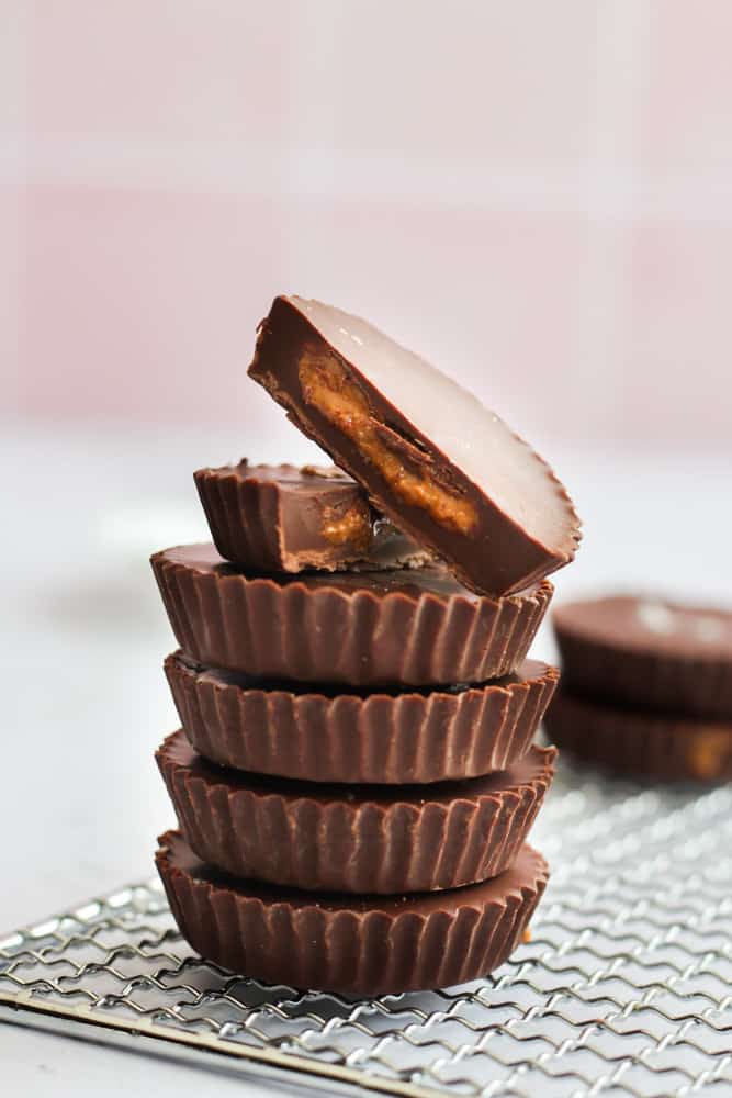 vegan almond butter cups stacked on top of each other. the top cup is cut in half so you can see the filling.