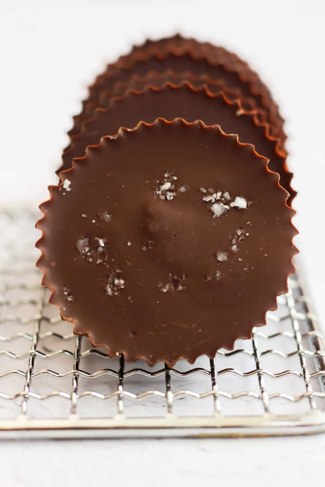 vegan almond butter cups lined up on a silver cooling rack, the front done is sprinkled with sea salt