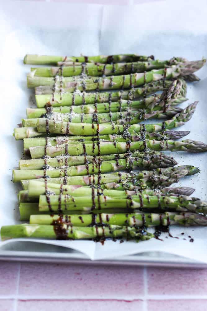 asparagus laid out on parchment paper and drizzled in a zig zag pattern with balsamic glaze