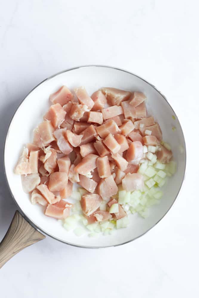 raw chicken and onion cooked in a white pan