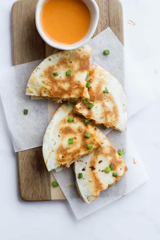 four quarters of buffalo chicken quesadilla on a wooden board lined with parchment paper