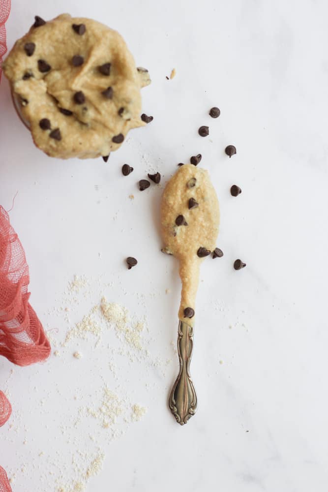 a spoonful of edible cookie dough on a white backdrop next to a jar full
