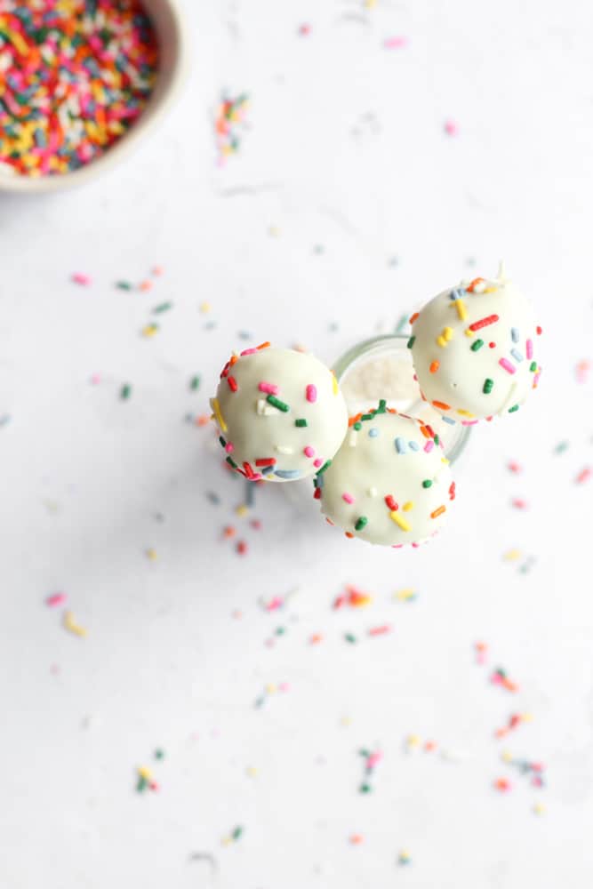 looking down on three white cake pops with sprinkles on a glass jar with sprinkles on the backdrop