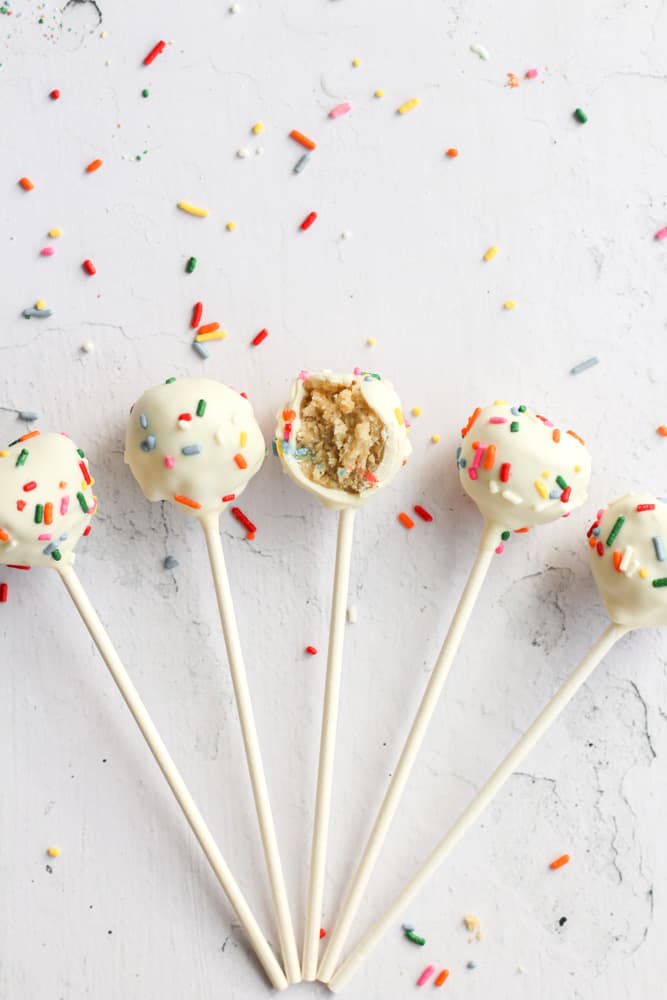 5 healthy cake pops on a white backdrop with sprinkles in an arch with a bite taken out of the middle one