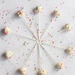 gluten free cake pops dipped in white chocolate and sprinkles displayed in a circle on a white backdrop littered with sprinkles