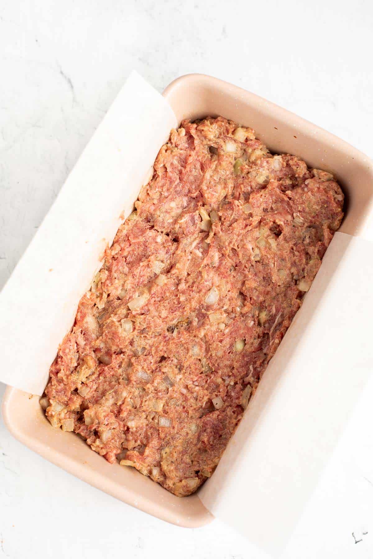 raw meatloaf mixture in a parchment lined loaf pan.