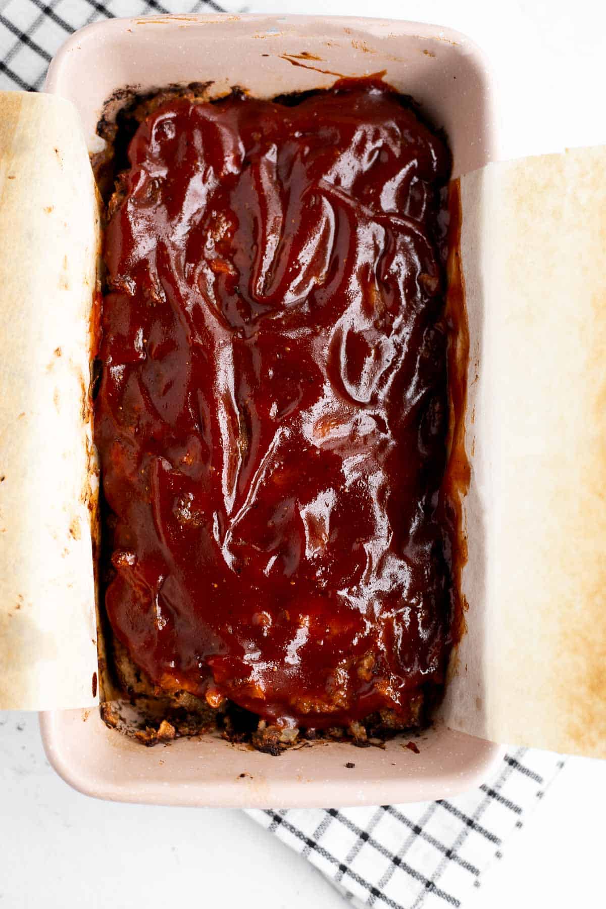 a glazed gluten free meatloaf in a parchment line loaf pan.